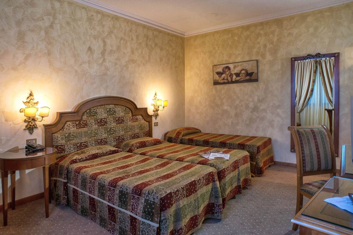 A hotel room with two beds, a nightstand, a chair, a TV, and a painting on the wall.