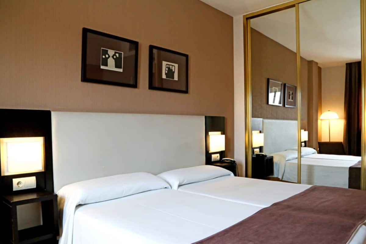 A hotel room with two beds, a large mirror, and framed pictures on the wall.