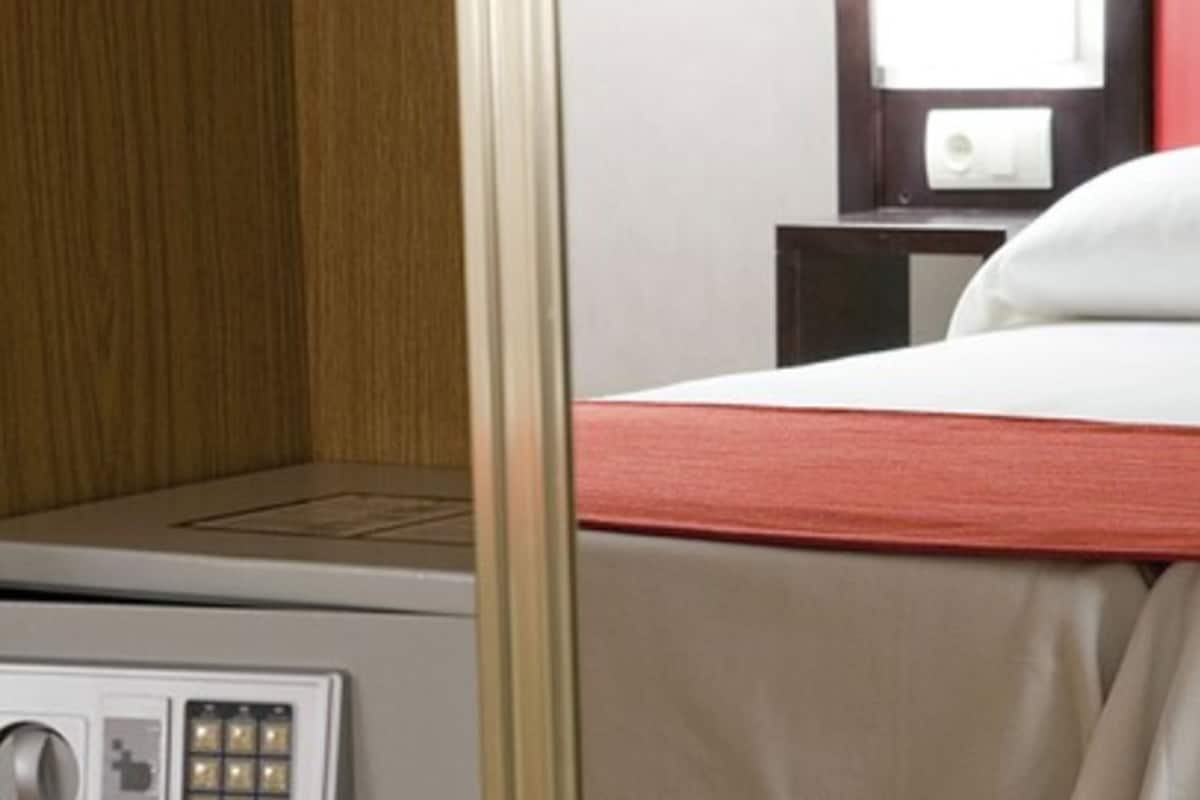 A hotel room with a bed, a control panel, and a small table with a lamp.
