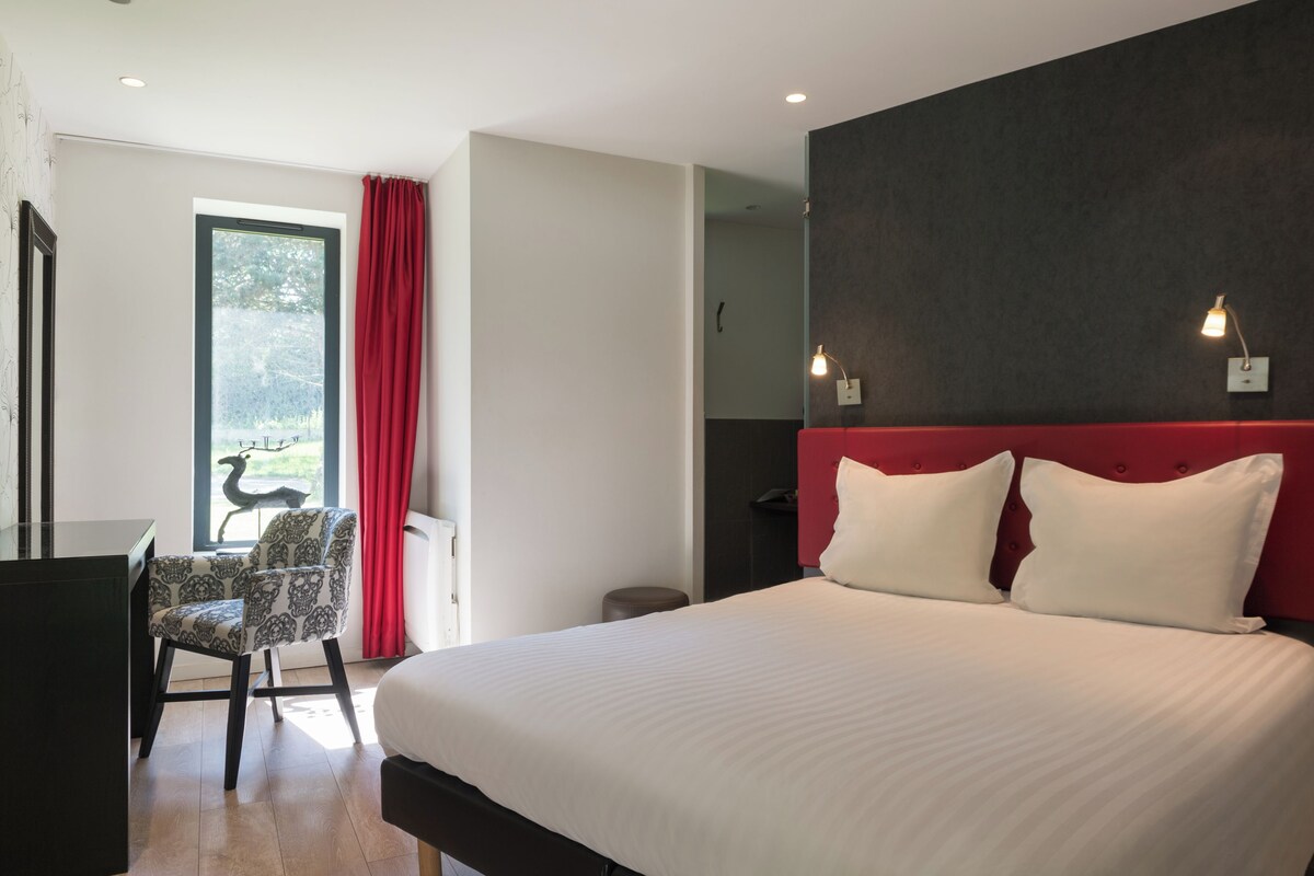 A hotel room with a large bed, a desk, a chair, and a window with curtains.