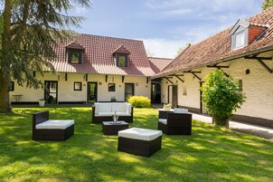 Um pátio com mobiliário de exterior, um edifício com telhado em azulejos e uma árvore.