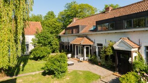 A two-story house with a tiled roof, a covered patio, and a garden with a lawn and trees.