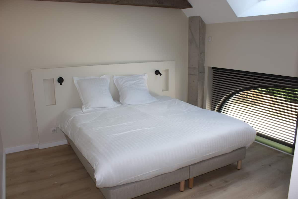 A bedroom with a bed, a skylight, and a window with blinds.
