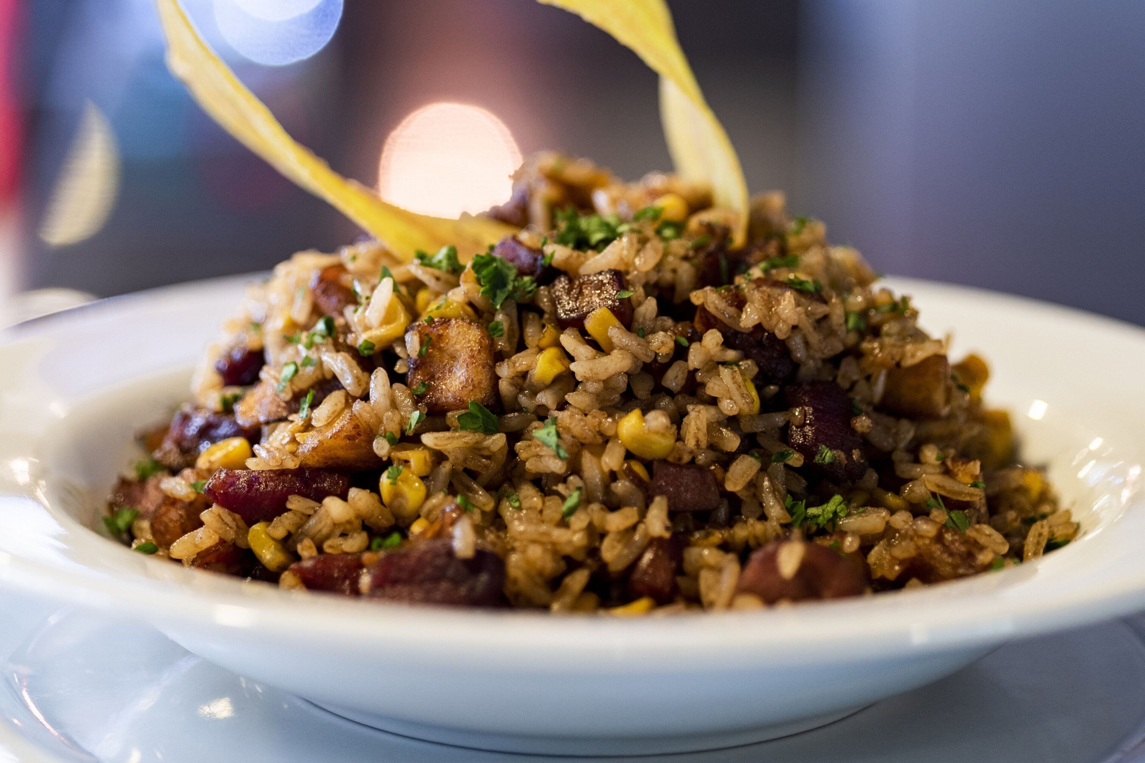 Uma tigela de arroz frito com ingredientes visíveis como milho, carne e ervas.