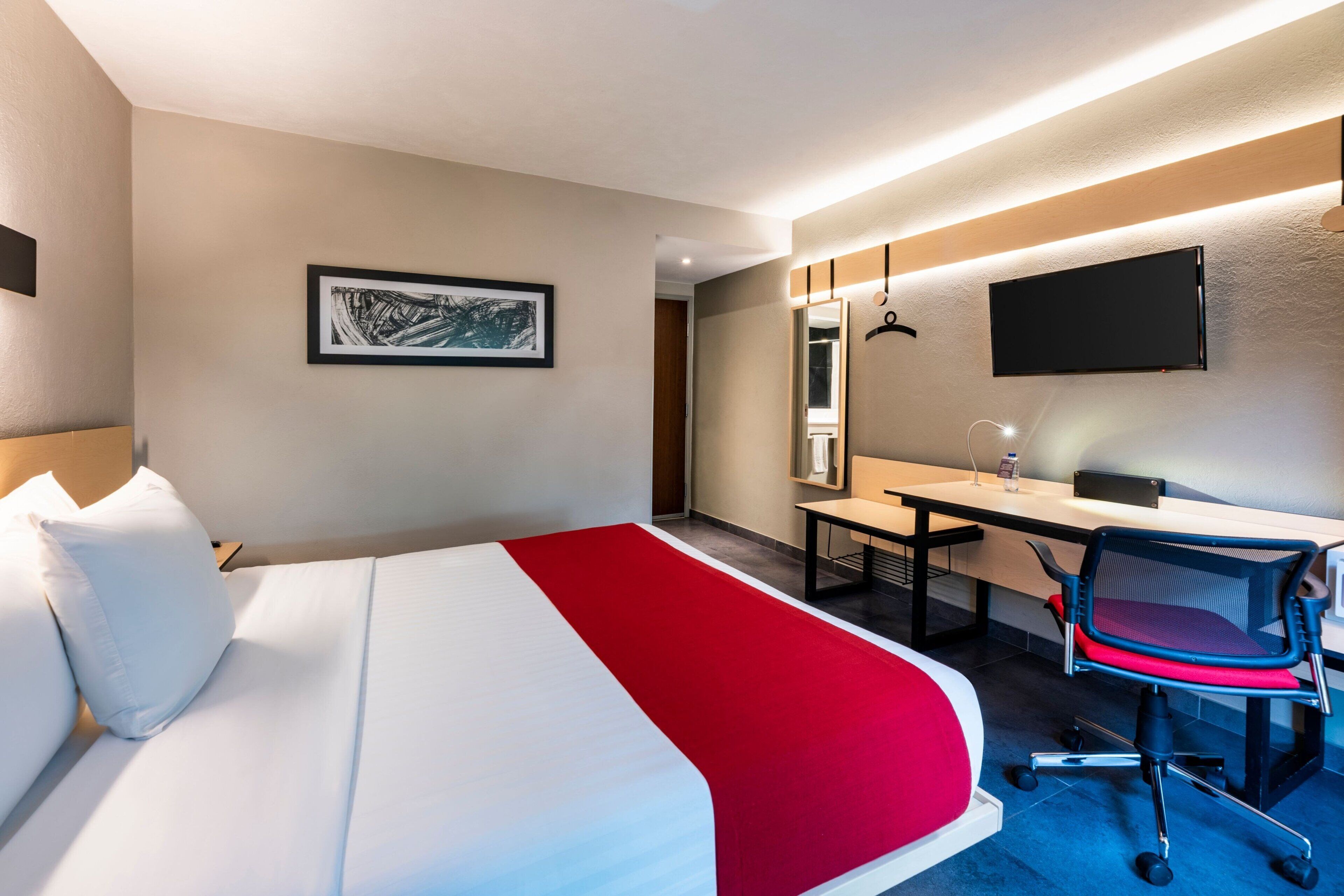 Een hotelkamer met een bed, een bureau, een stoel, een flatscreen-televisie en een lijst aan de muur.