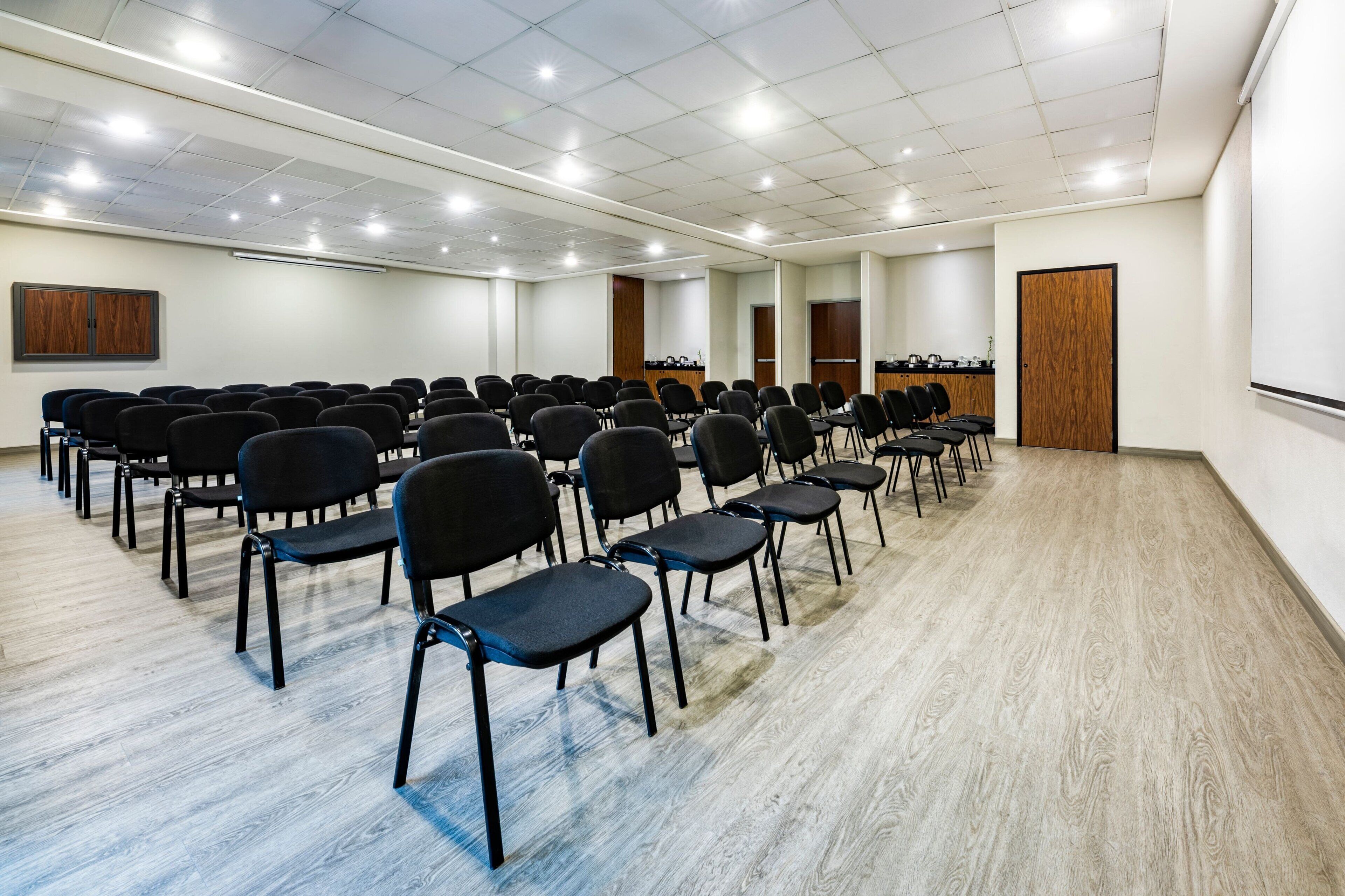 A conference room with rows of black chairs, wooden paneling on the walls, and a whiteboard.