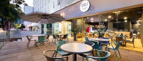 An outdoor seating area with tables and chairs, a large umbrella, and a Deli sign on the building.