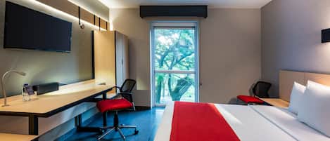 A modern hotel room with a bed, desk, chairs, and a TV.