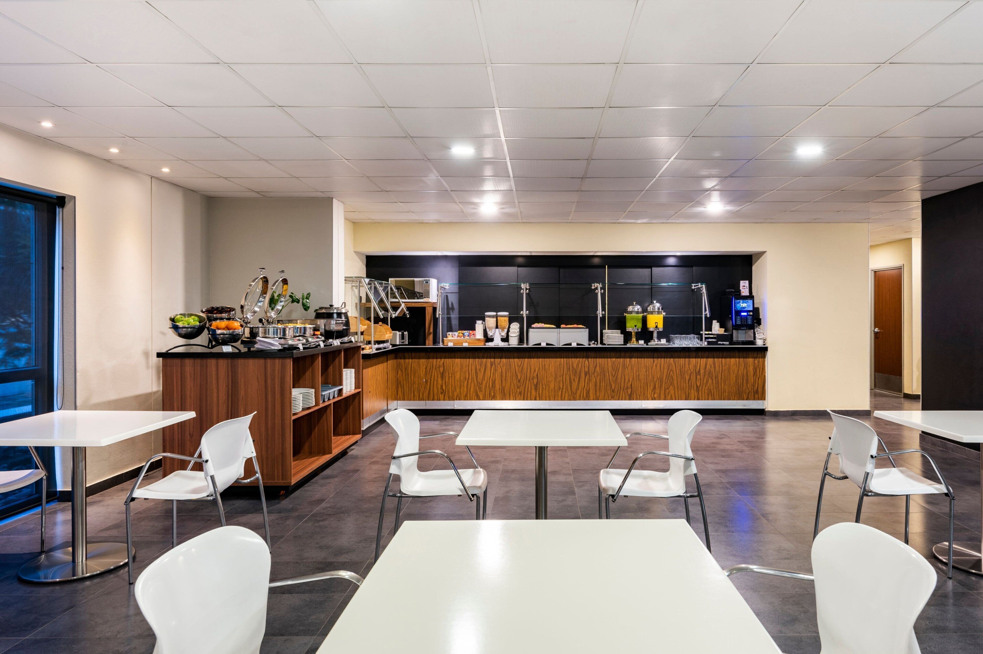 A modern cafe with a counter, white chairs, and tables.