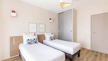 Ein Hotelzimmer mit zwei Einzelbetten, einem Holzkopfteil, einer Tür und einer Leuchte.