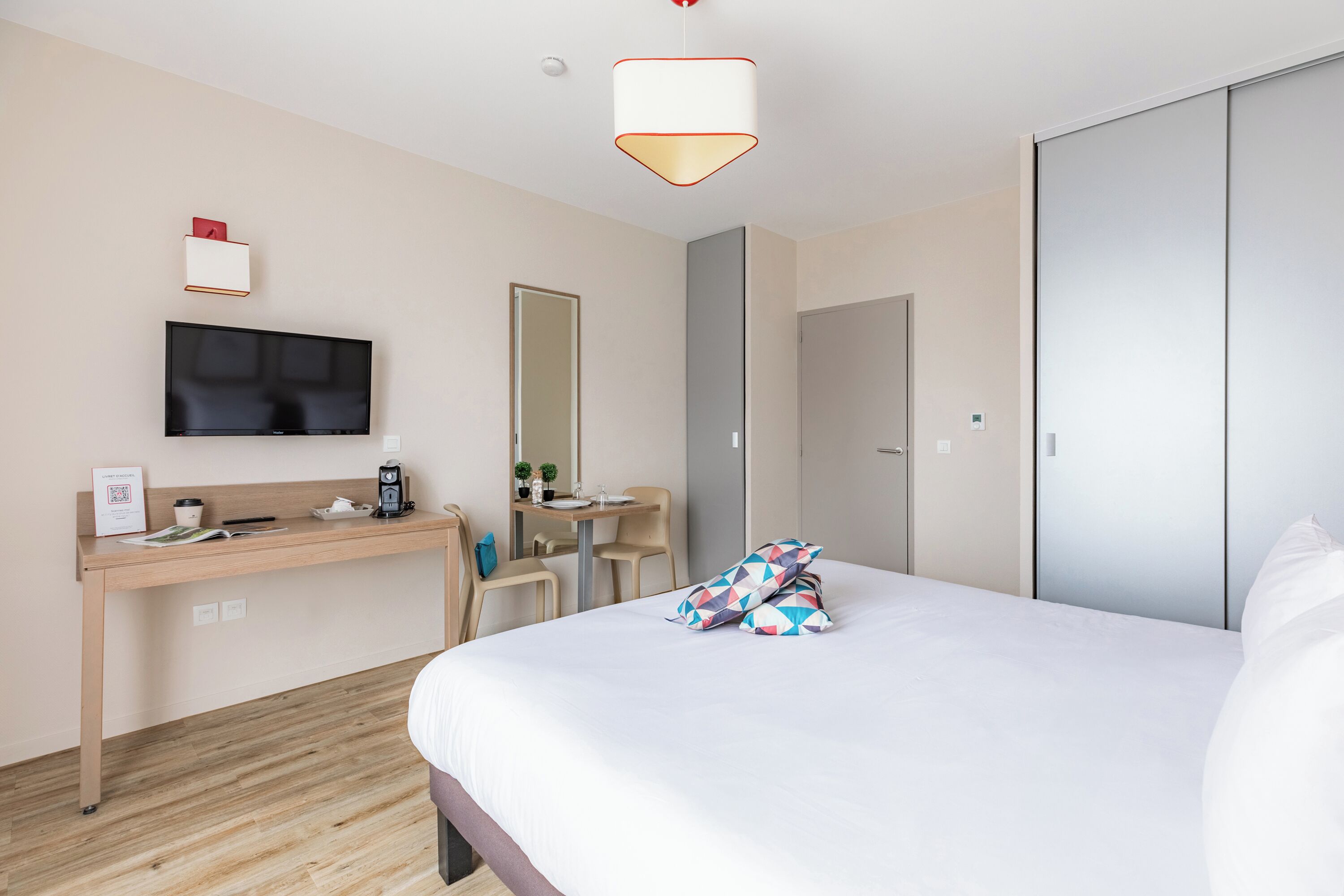 Habitación de hotel con cama, escritorio con silla, televisión, espejo y armario.