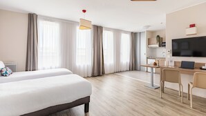 Ein Hotelzimmer mit Bett, Schreibtisch, Stühlen, einem Fernseher und einer Küchenzeile.