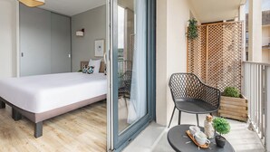 Ein modernes Schlafzimmer mit einem Bett, einem Sessel und einem kleinen Tisch mit Pflanze und Dekoration.