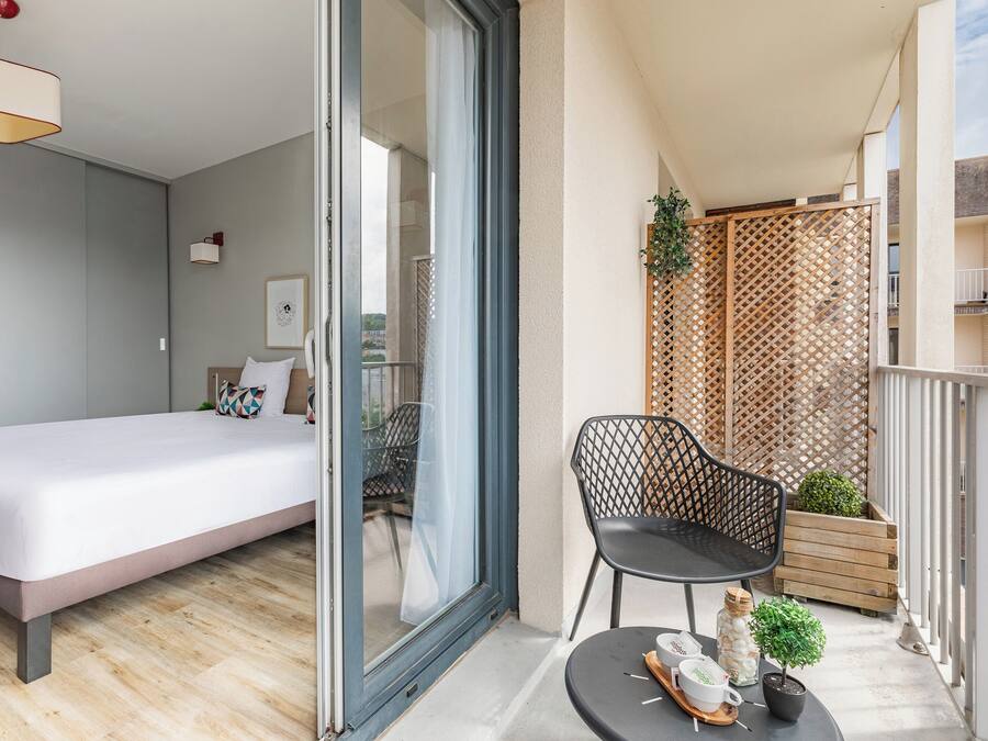 A modern bedroom with a bed, a chair, and a small table with a plant and a decorative item.