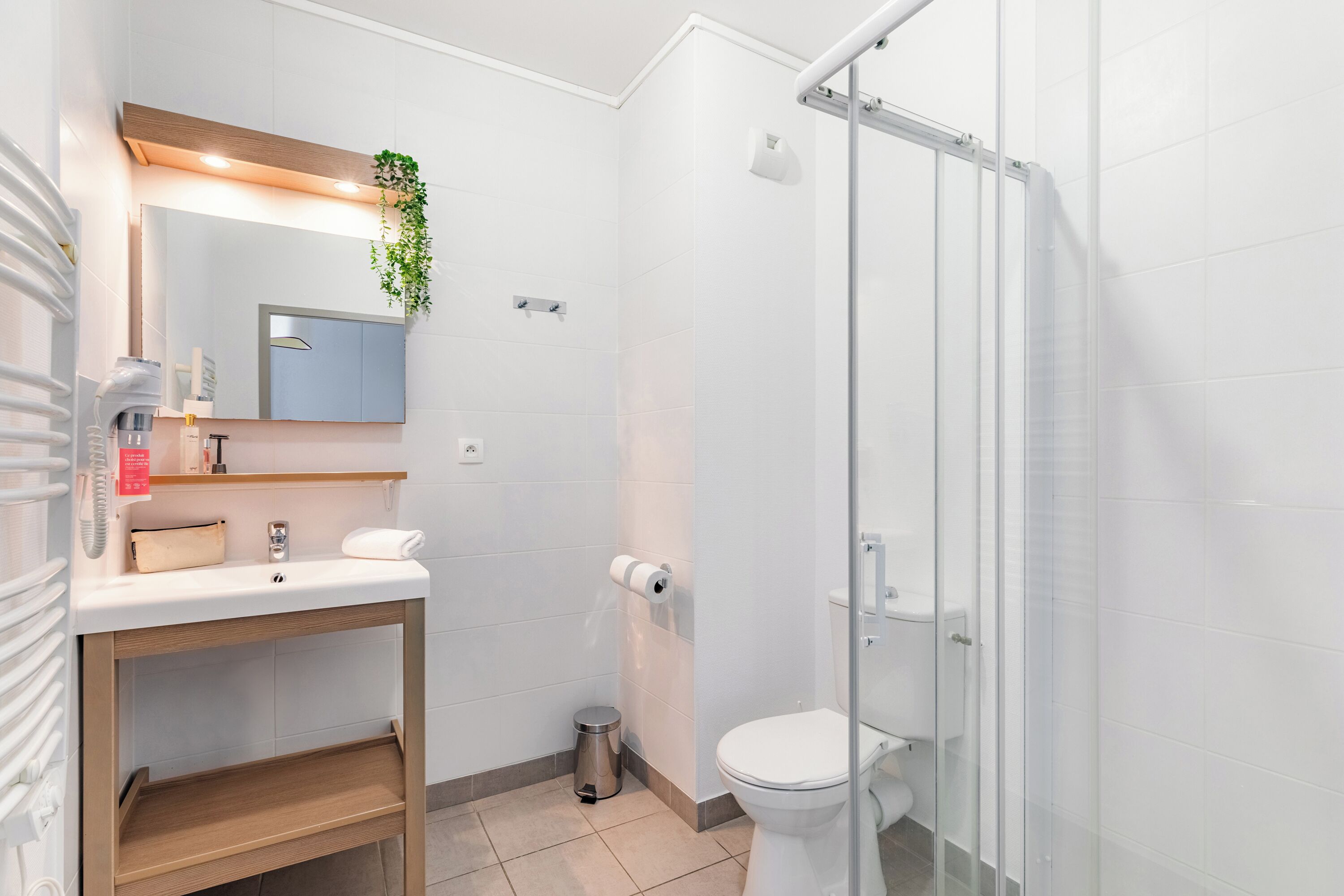 Ein modernes Badezimmer mit einer Duschkabine aus Glas, einem weißen Waschbecken mit Spiegel darüber und einer kleinen Mülleimer.