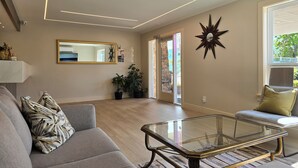 A modern living room with a glass coffee table, grey sofa, and potted plants. - Sahara Courtyard Inn (Osoyoos)