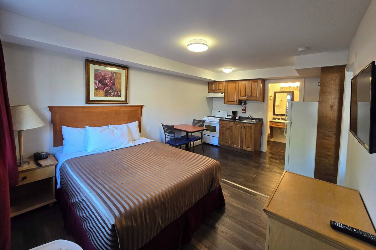 A hotel room with a bed, bedside table, lamp, and a painting on the wall.