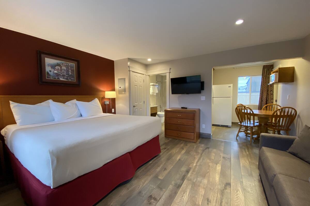 A hotel room with a large bed, a dresser, a television, a dining table with chairs, and a small sofa.