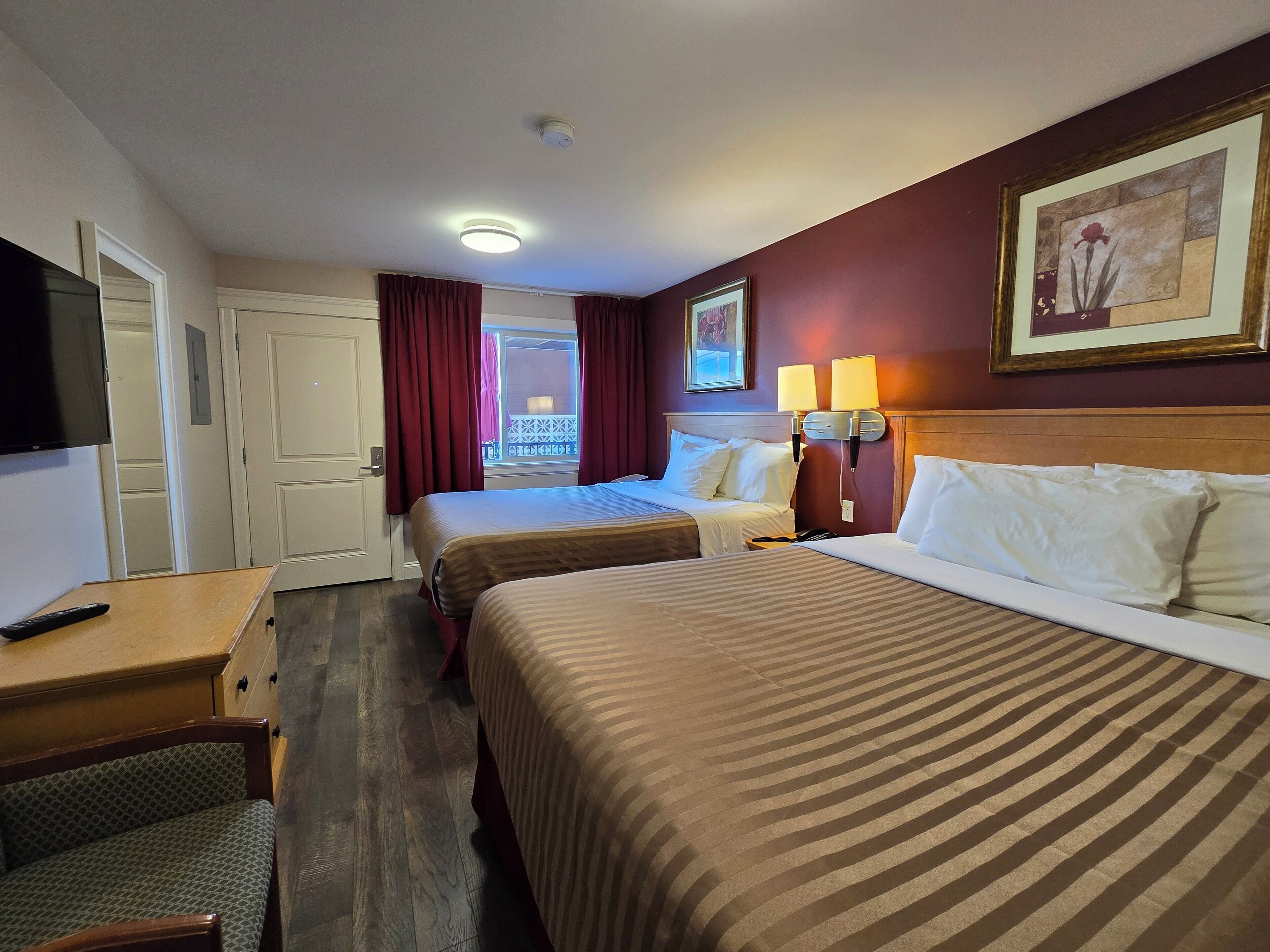A hotel room with two beds, a desk, a chair, a TV, and a balcony with curtains.