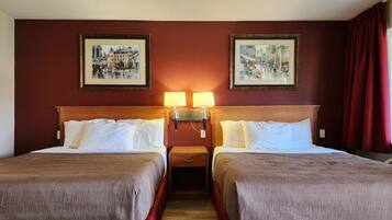 A hotel room with two beds, a wooden headboard, two wall-mounted lamps, and two framed pictures on the wall.