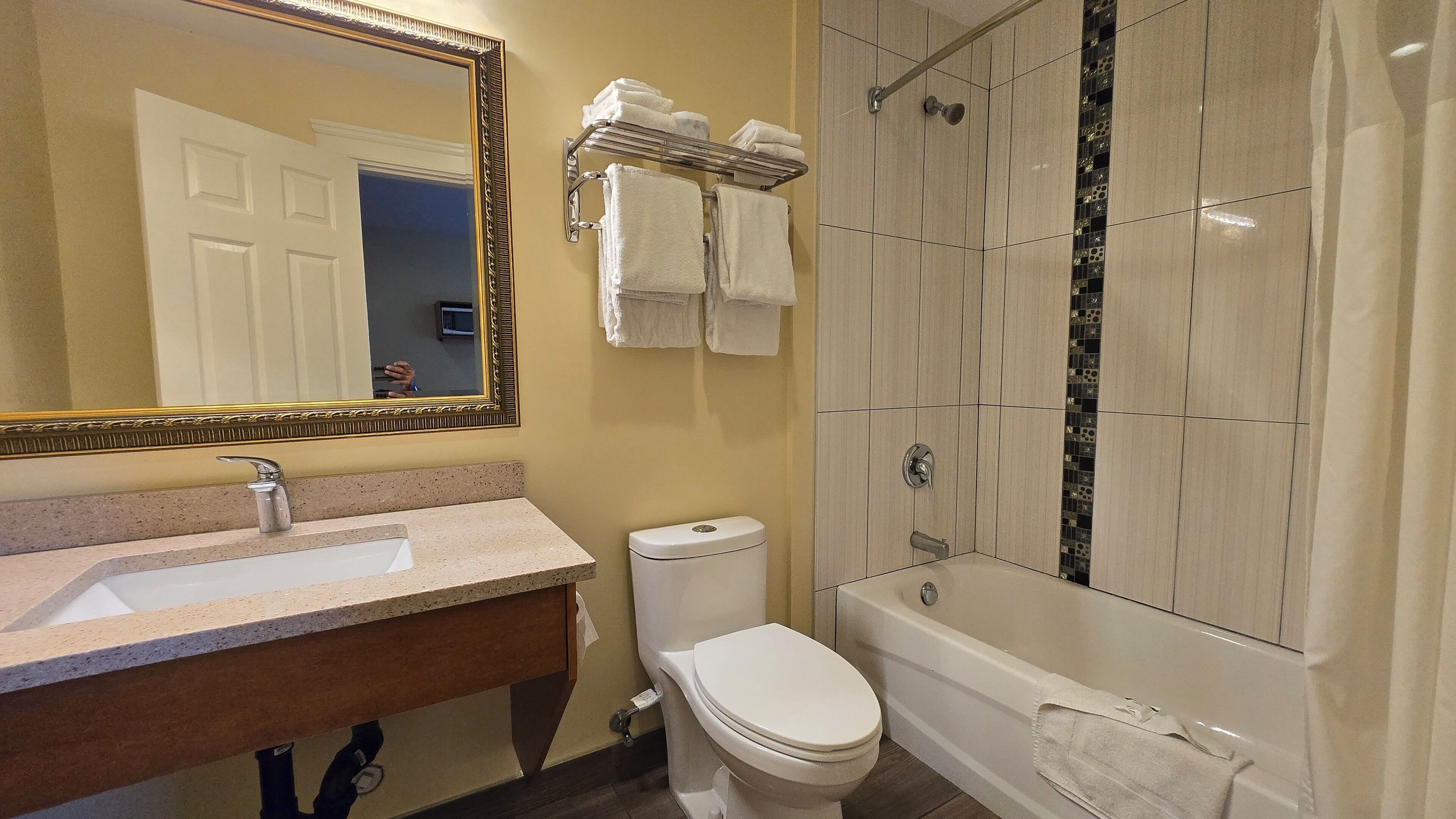 A bathroom with a sink, toilet, and bathtub. There is a mirror with a decorative frame, and towels are hung on a rack.