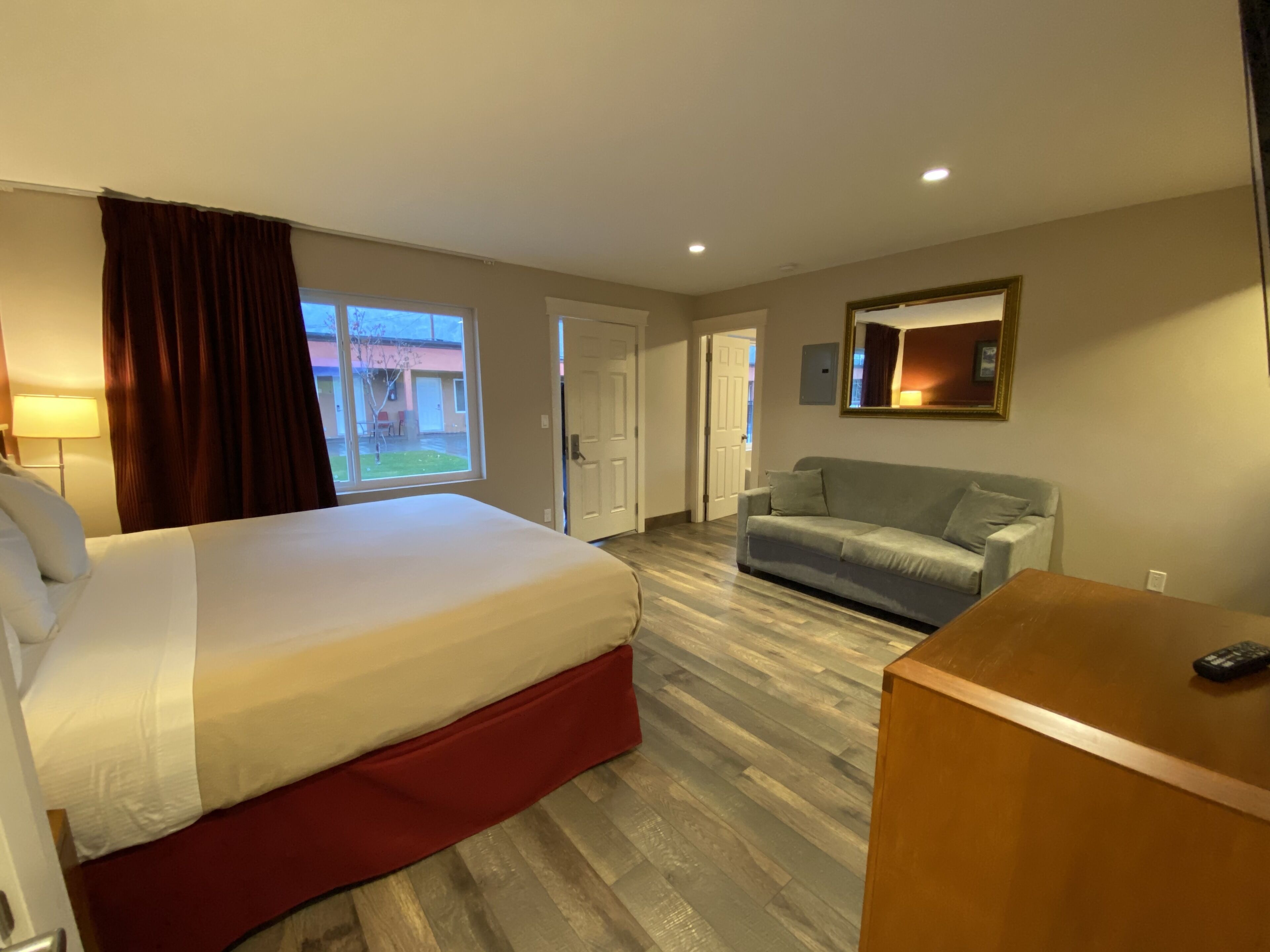 A hotel room with a bed, a desk, a sofa, a window, and a door.