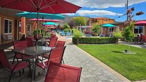 An outdoor patio with tables and chairs, umbrellas, and a pool area. - Sahara Courtyard Inn (Osoyoos)