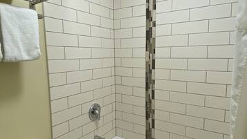 A bathroom with a white bathtub, a toilet, and a shower area with white tiles and a mosaic strip.