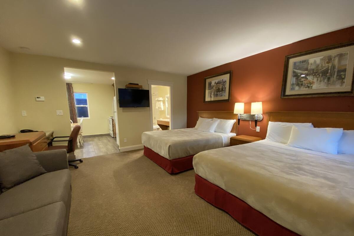 A hotel room with two beds, a desk, a chair, and a television.
