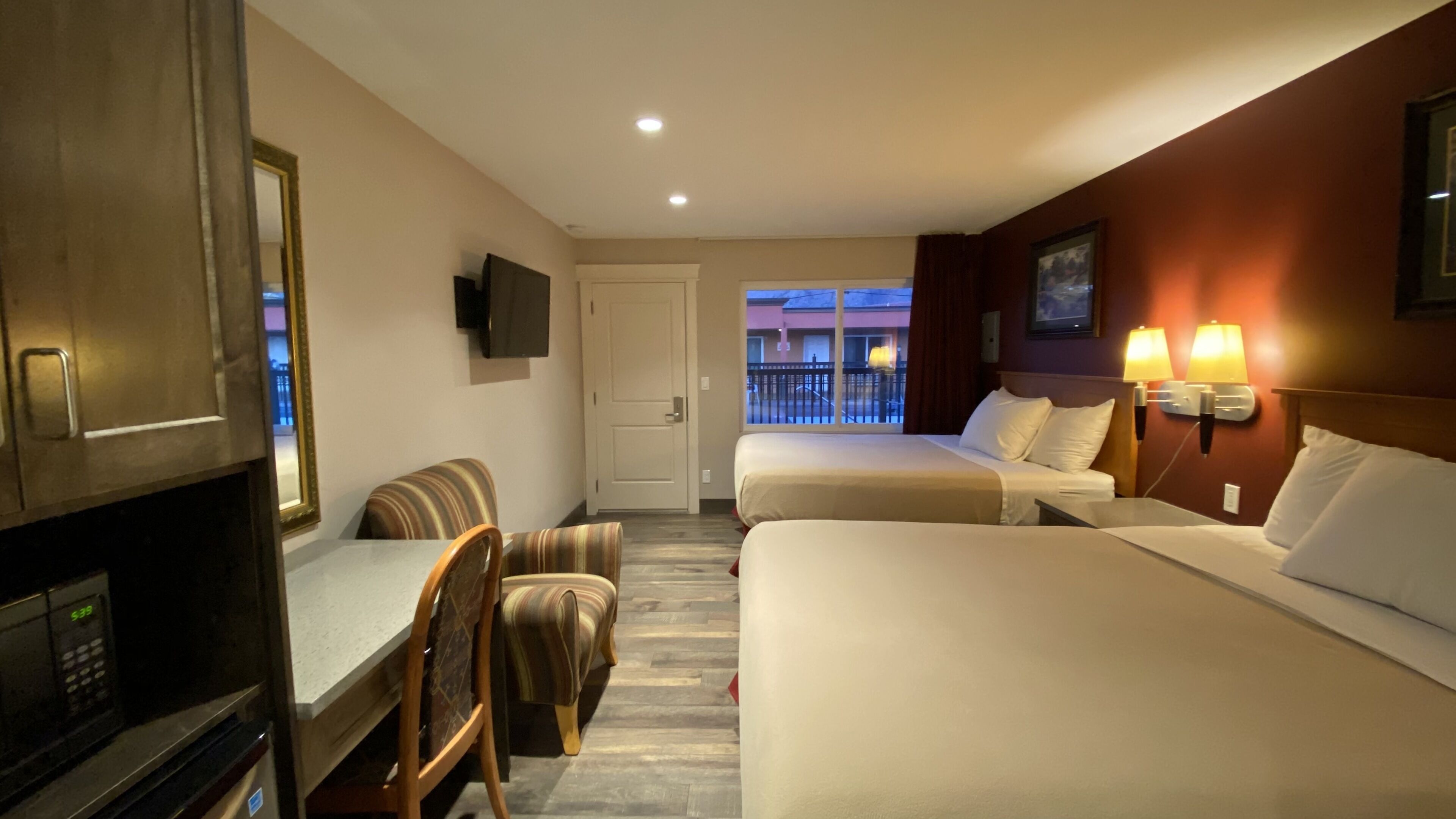 Une chambre d’hôtel avec deux lits, une table à manger, des chaises, un téléviseur et une vue sur le balcon extérieur.
