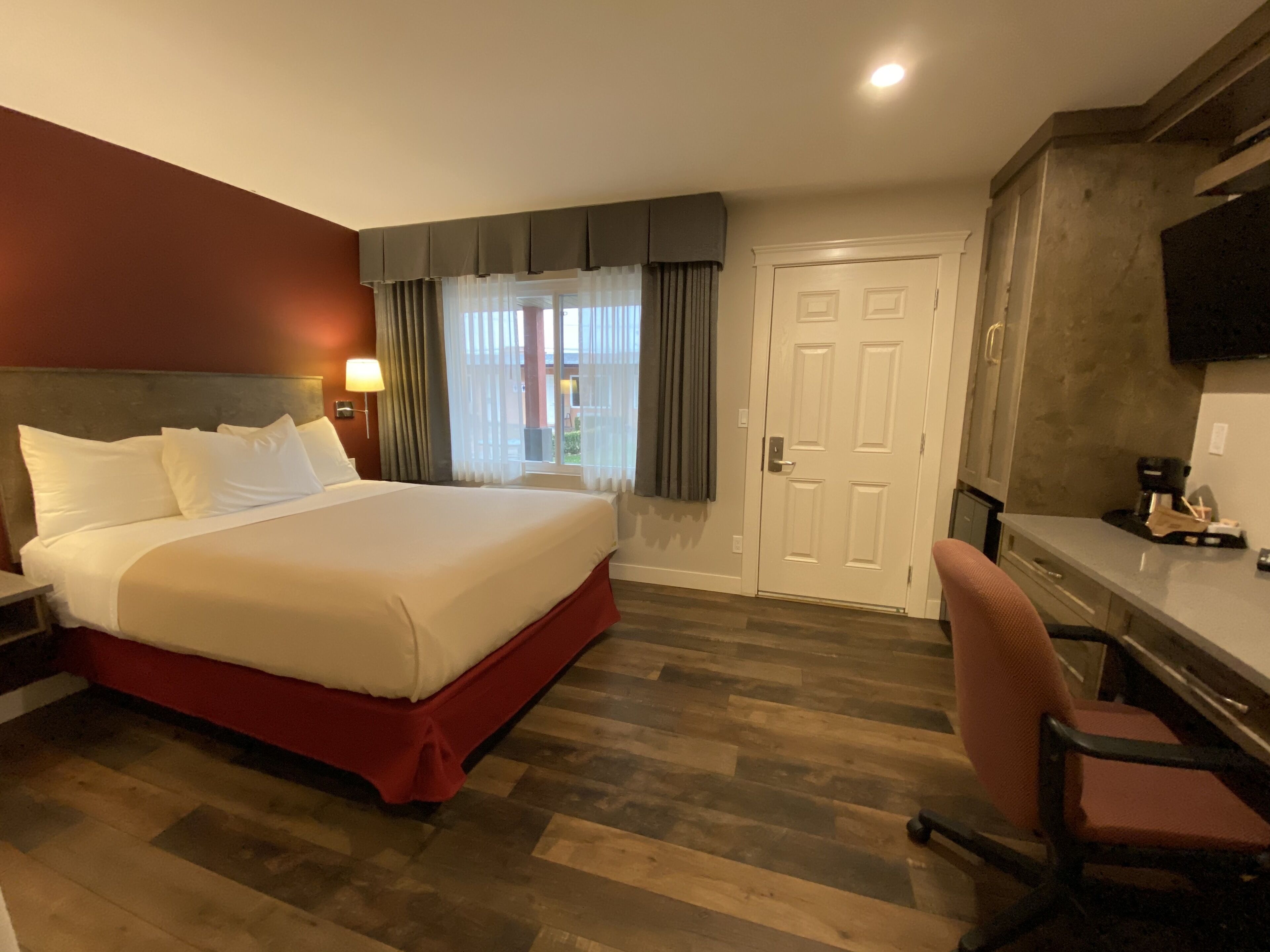 A hotel room with a large bed, a desk with a chair, a television, and a door.