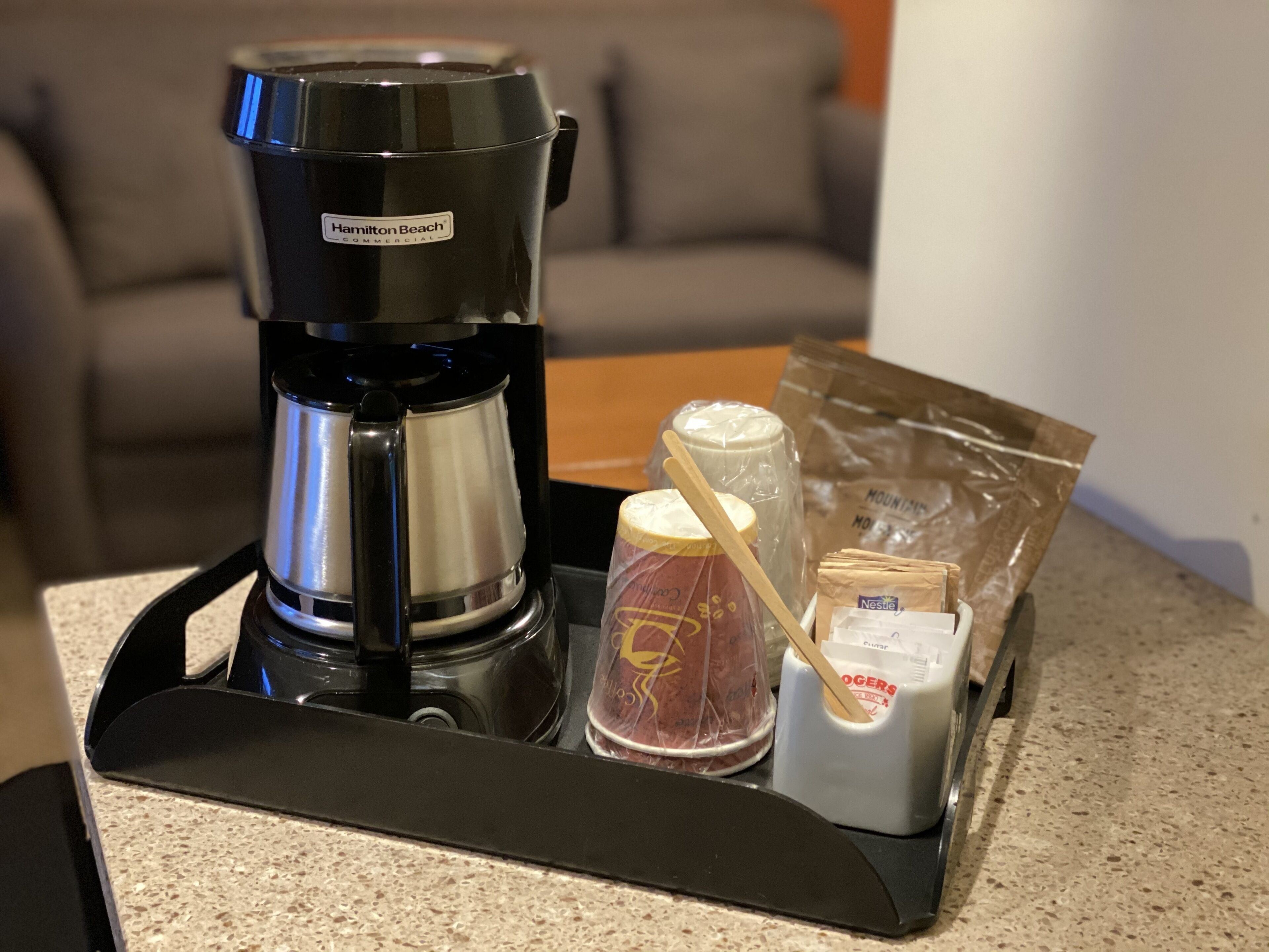 Eine Kaffeemaschine, eine Packung Kaffeekapseln, Zucker und ein Sahneerset auf einer Arbeitsfläche.