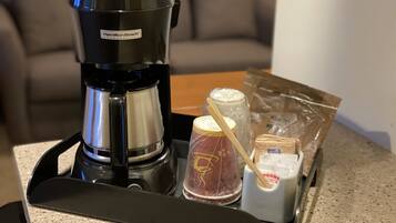 Eine Kaffeemaschine, eine Packung Kaffeekapseln, Zucker und ein Sahneerset auf einer Arbeitsfläche.
