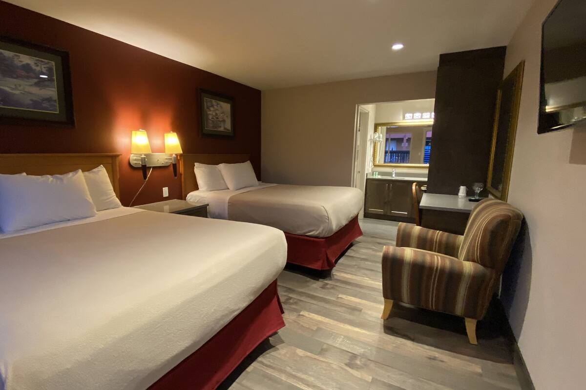 A hotel room with two beds, a chair, and a mirror.