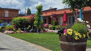 A hotel courtyard with a paved walkway, potted plants, and a row of buildings with red awnings. - Sahara Courtyard Inn (Osoyoos)