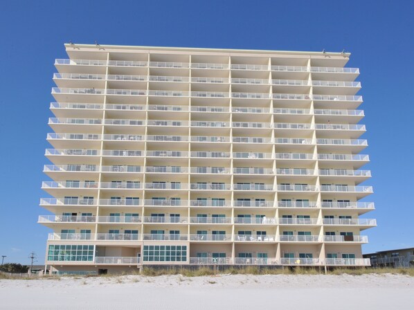 A multi-story hotel with balconies, a beach view, and a sandy ground floor.