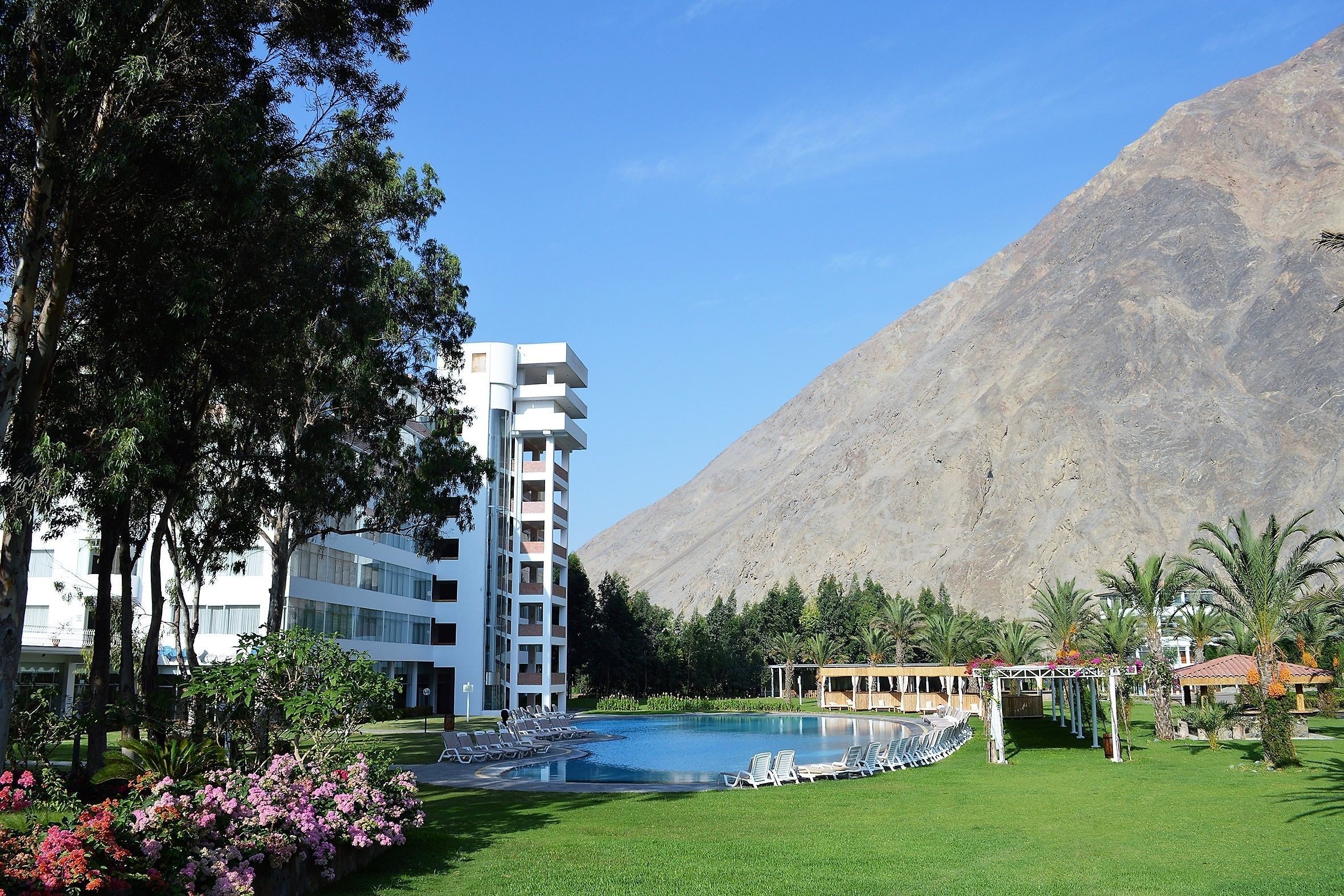 A hotel with a pool, surrounded by greenery and a mountain backdrop.