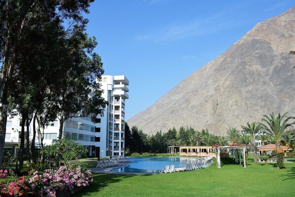 A hotel with a pool, surrounded by greenery and a mountain backdrop.