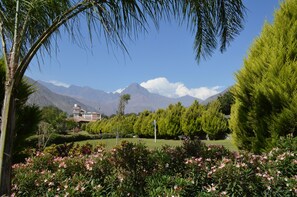 A landscaped garden with a view of mountains and a building with a dome roof. - Guizado Portillo Hacienda & Resort (Pacarán)