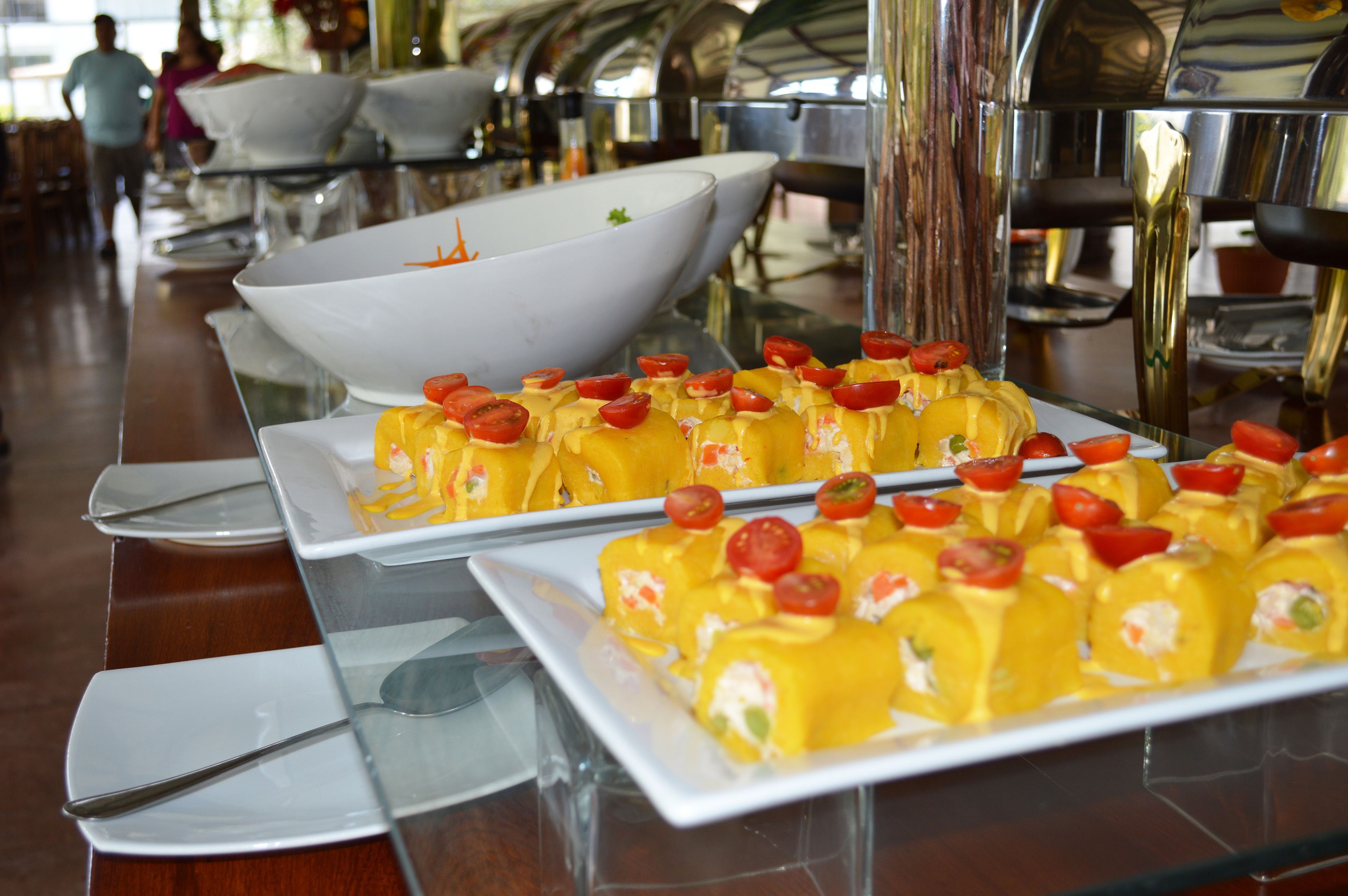 A buffet table with yellow food items and a large white bowl in the background.