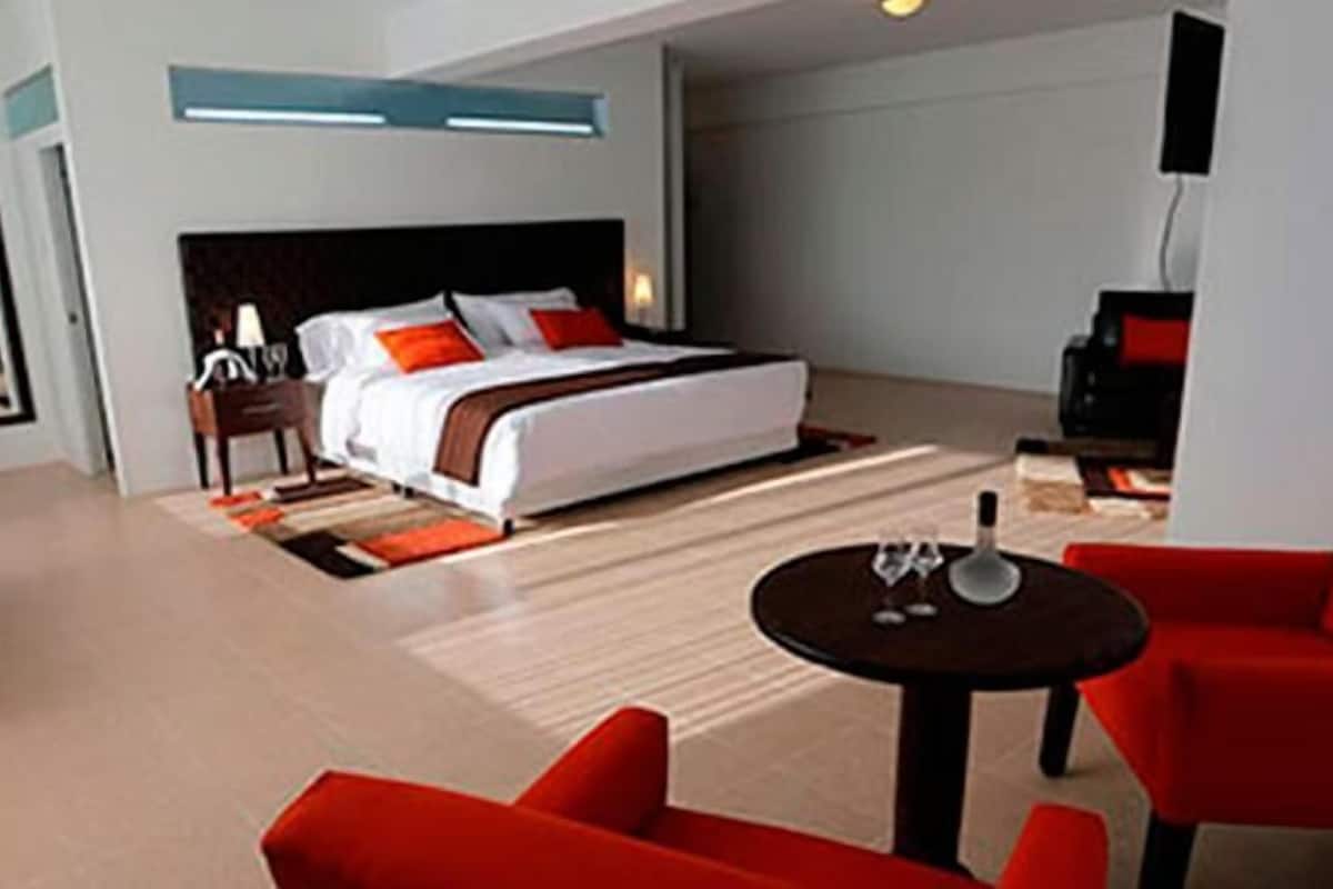 Ein modernes Hotelzimmer mit einem großen Bett, roten Sesseln, einem kleinen Tisch und einem Fernseher.