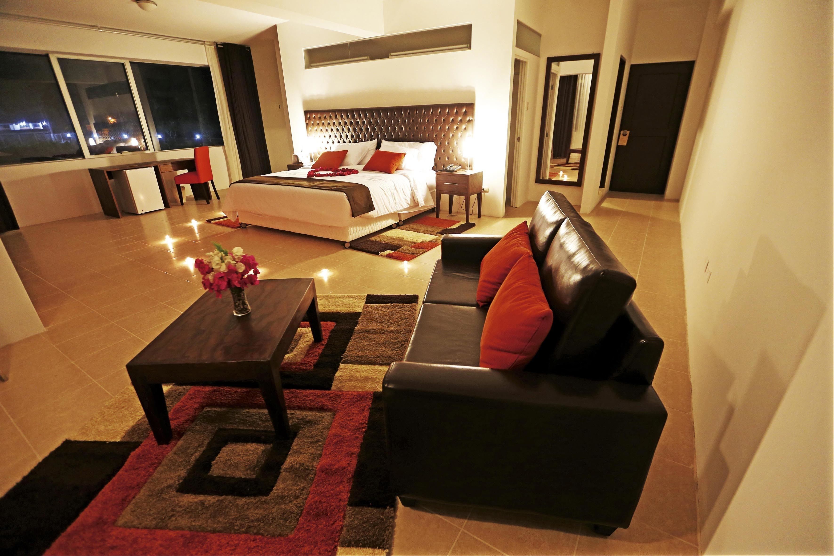 A modern hotel room with a large bed, a sofa, a desk, and a view of the city at night.