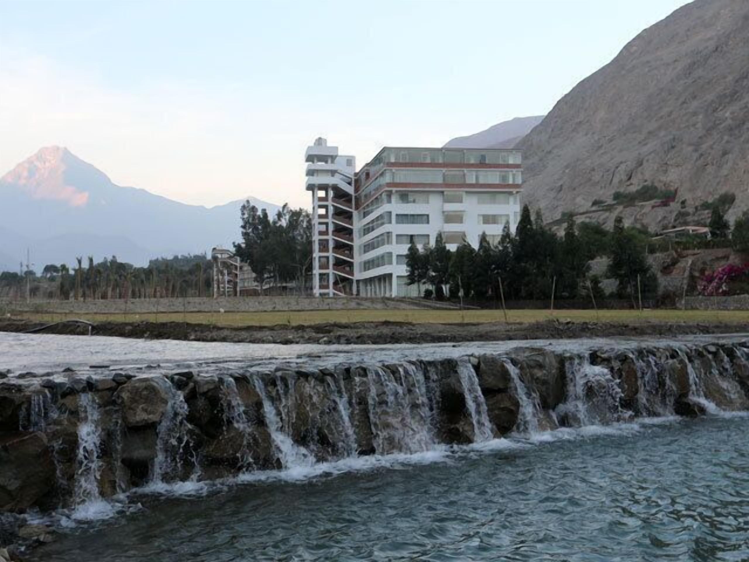 A multi-story hotel with a modern design, located near a waterfall and mountains.