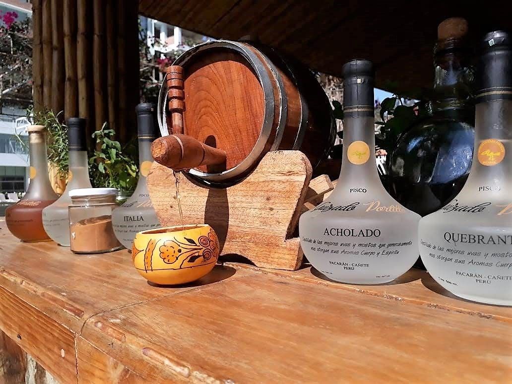 A wooden barrel, two bottles labeled 'Pisco', and a small bowl with a floral design.