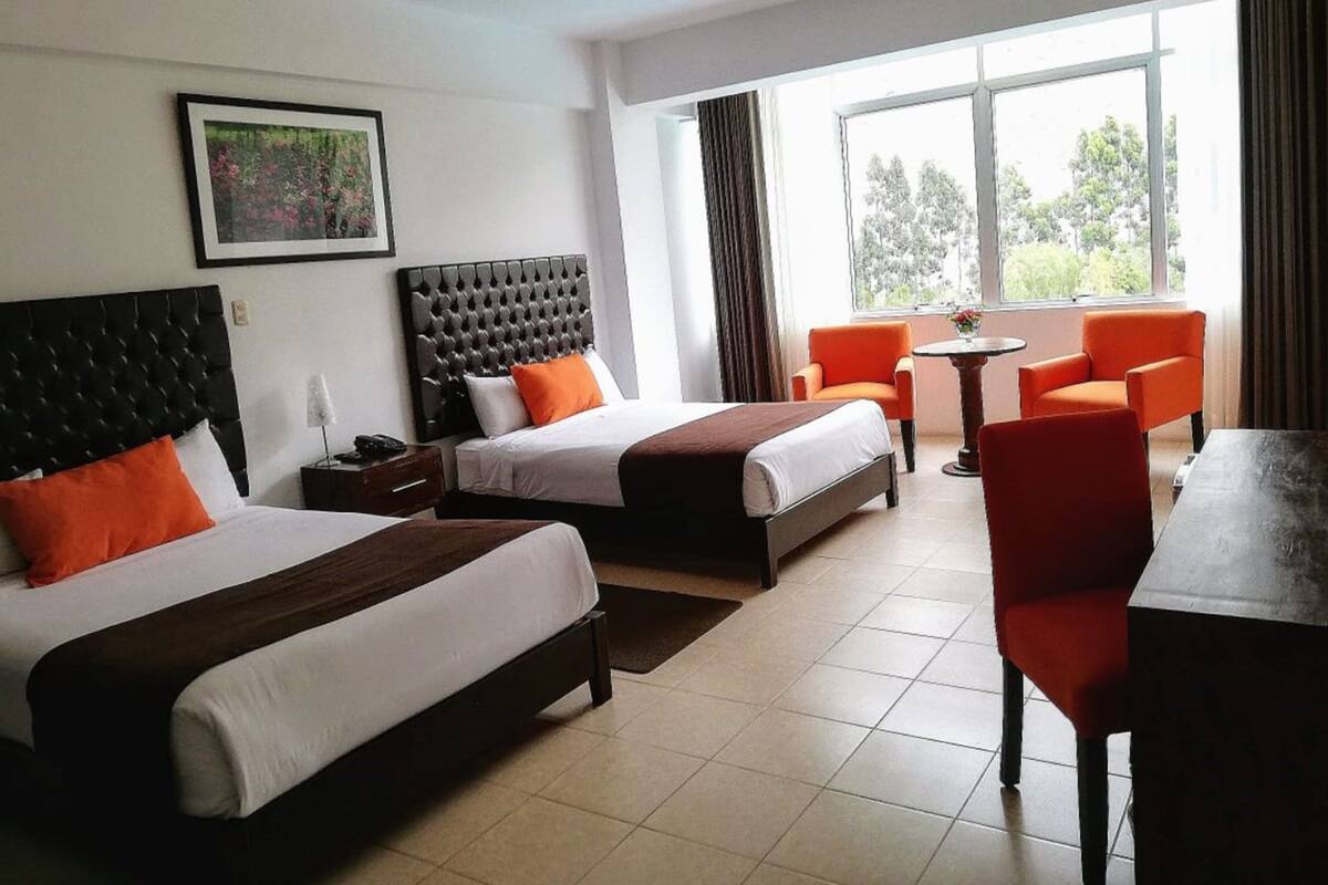 Ein Hotelzimmer mit zwei Betten, einem Esstisch und einem Fenster mit Vorhängen.