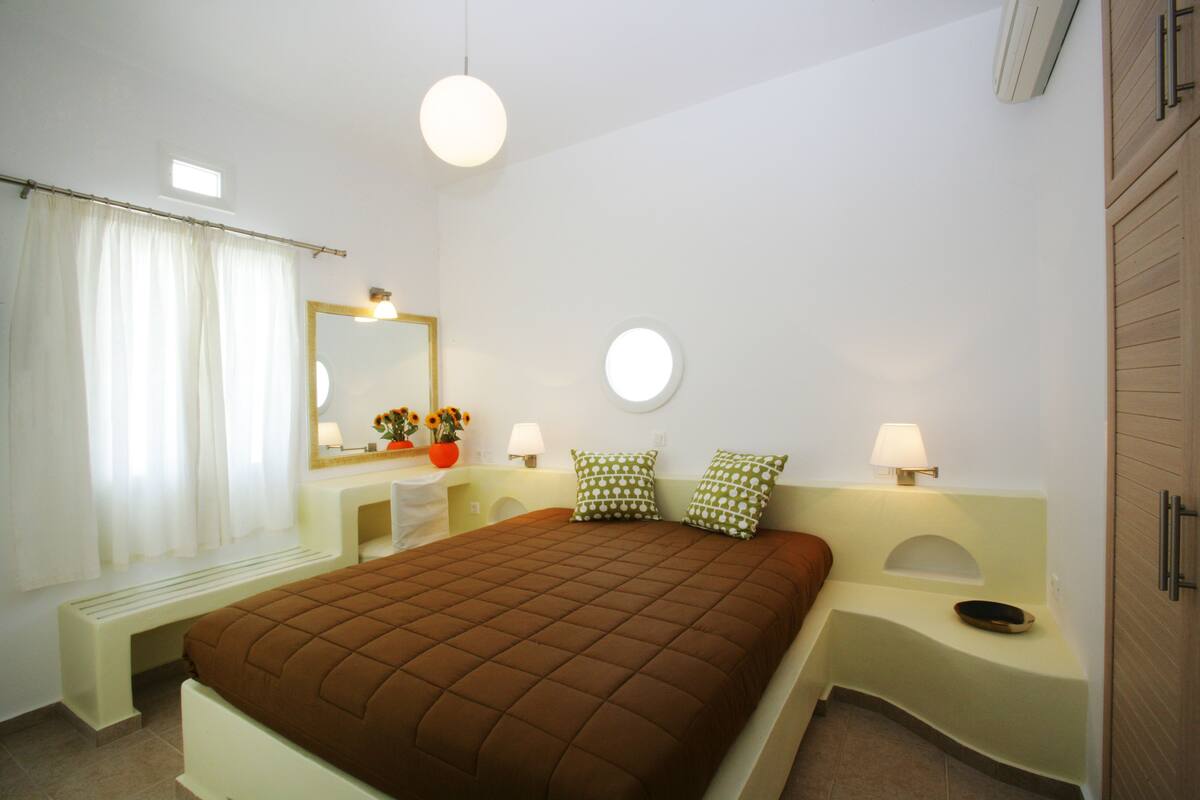 Un dormitorio con cama, mesitas de noche, un espejo y una ventana con cortinas.