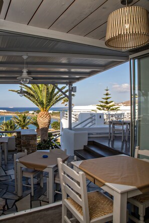 Um terraço com móveis brancos, uma palmeira e vista para o mar.