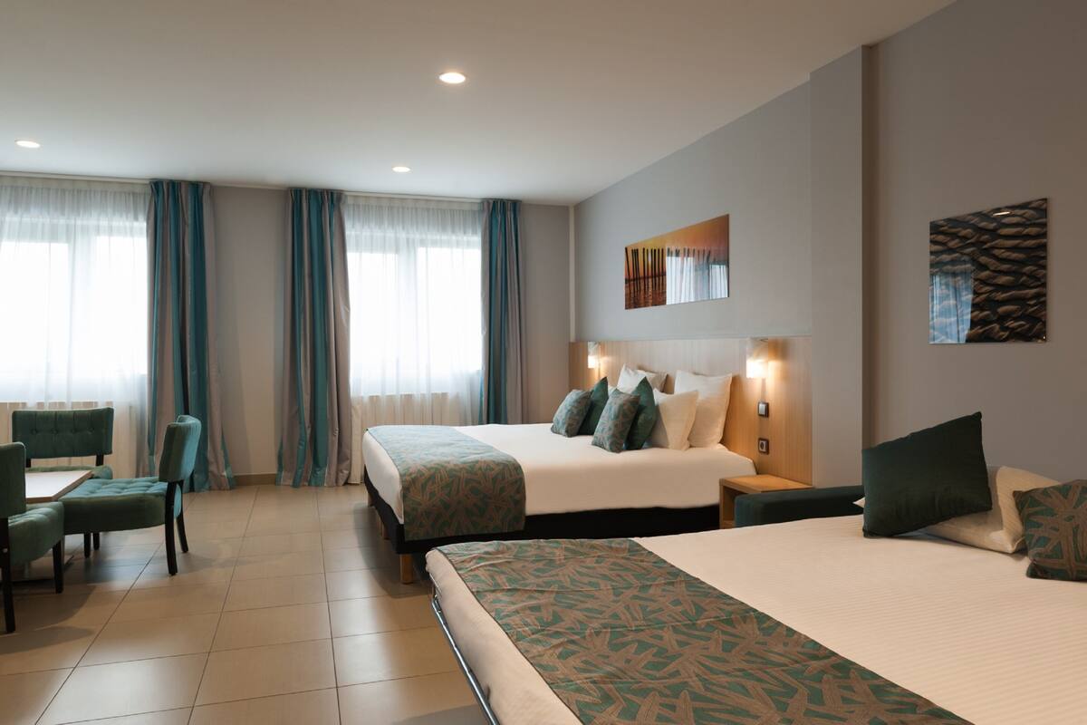 Une chambre d’hôtel avec un grand lit, un bureau avec une chaise et une fenêtre avec des rideaux.