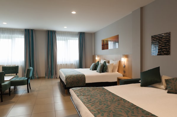 A hotel room with a large bed, a desk with a chair, and a window with curtains.