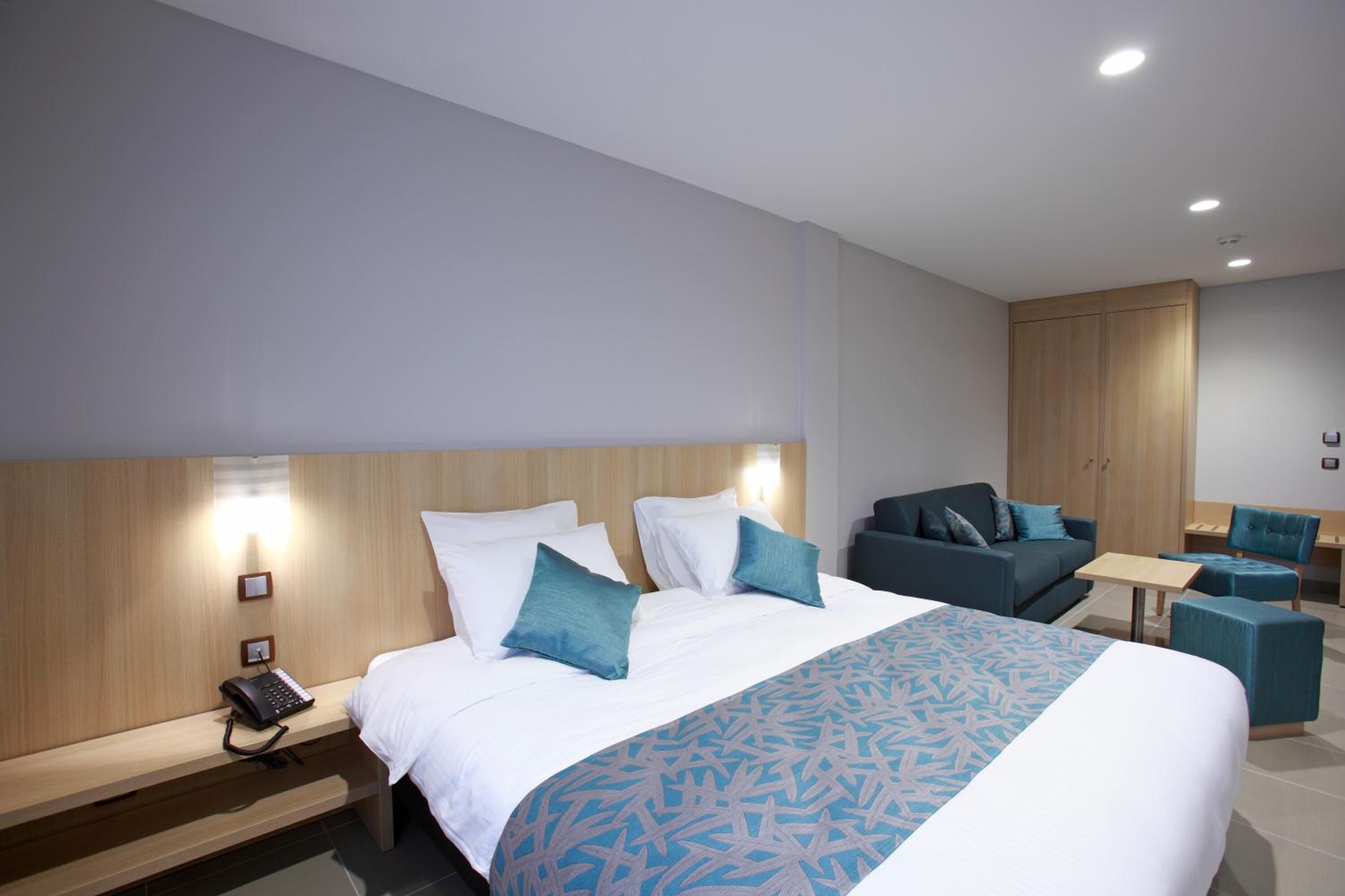 A modern hotel room with a large bed, a desk, a sofa, and a wardrobe.